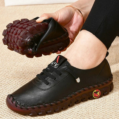 Black leather shoe with brown sole held by a hand on a beige background