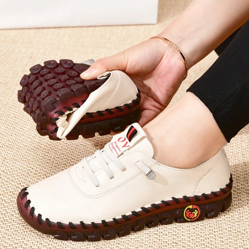 White shoe with red sole held by a hand on a textured surface