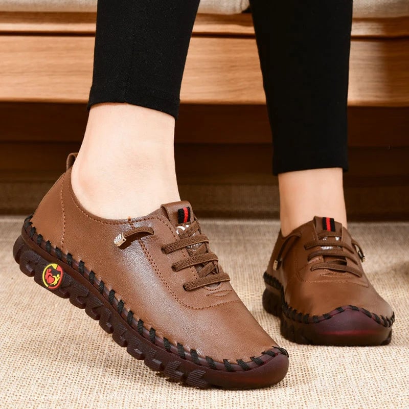 Brown leather shoes worn with black pants on a wooden floor.
