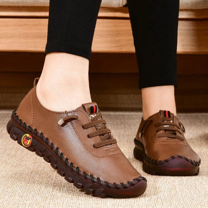 Brown leather shoes worn with black pants on a wooden floor.