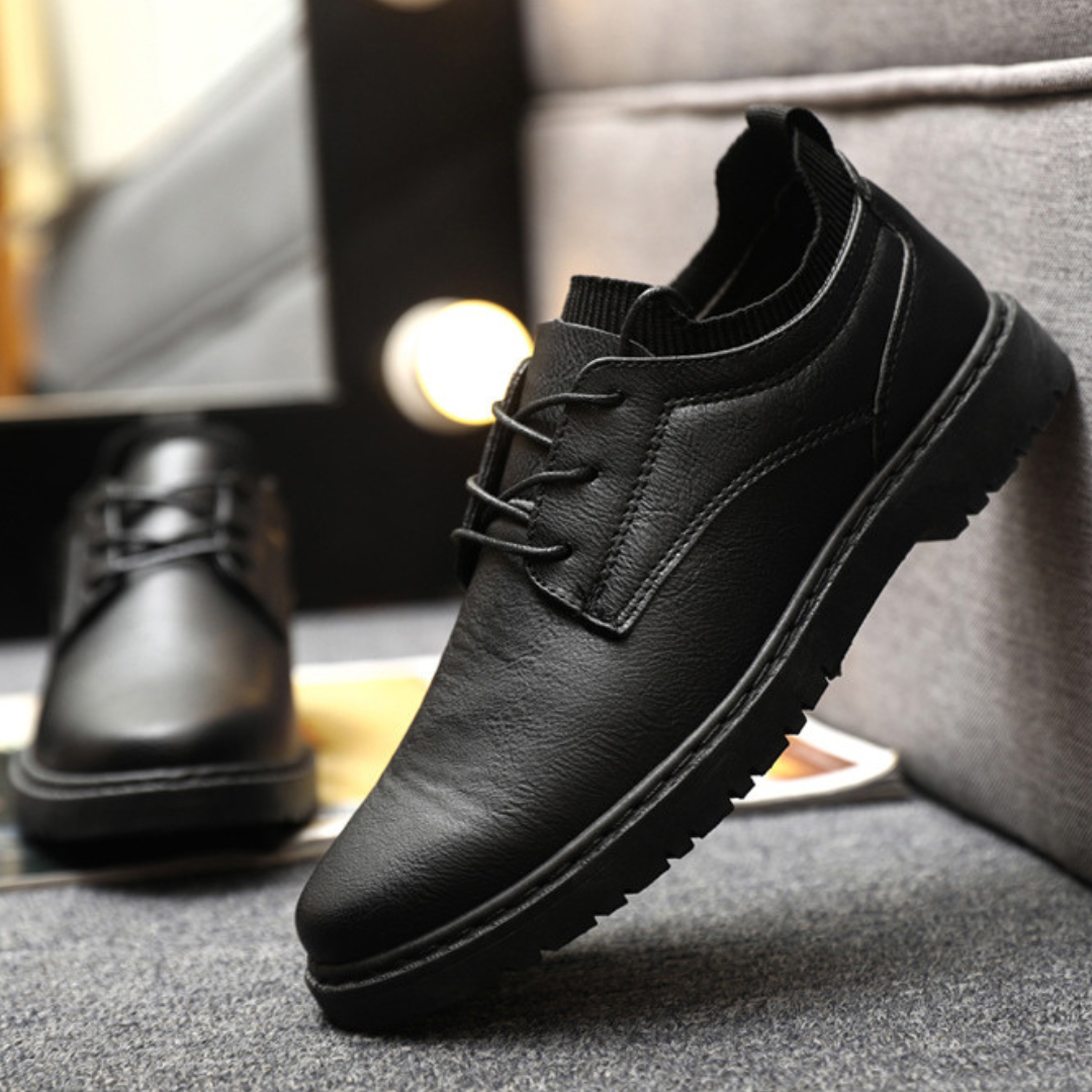 Black leather shoes on a gray surface with blurred lights in the background