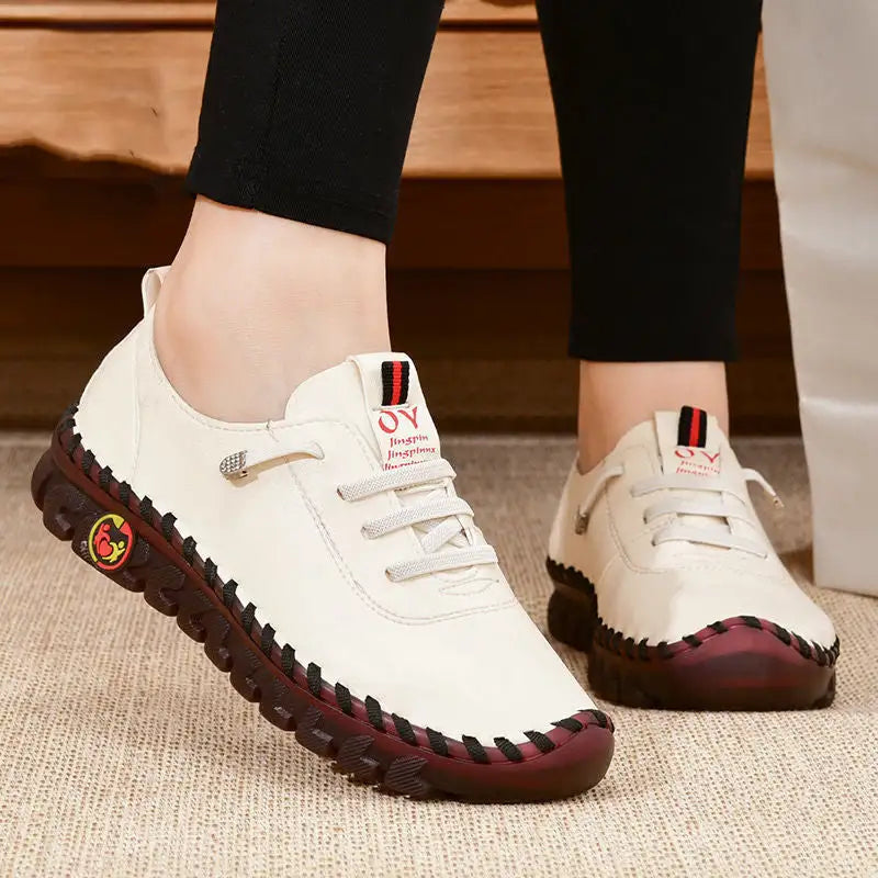 White sneakers with red soles worn by a person on a wooden floor.