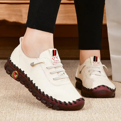 White sneakers with red soles worn by a person on a wooden floor.