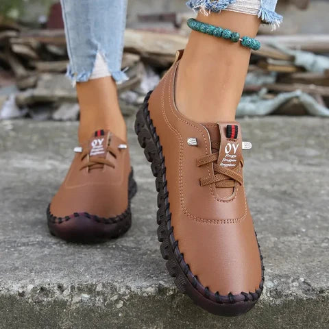 Brown leather shoes with brand logo worn by a person on a concrete surface.