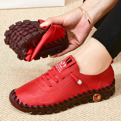 Red shoes with black soles held by a hand on a textured surface